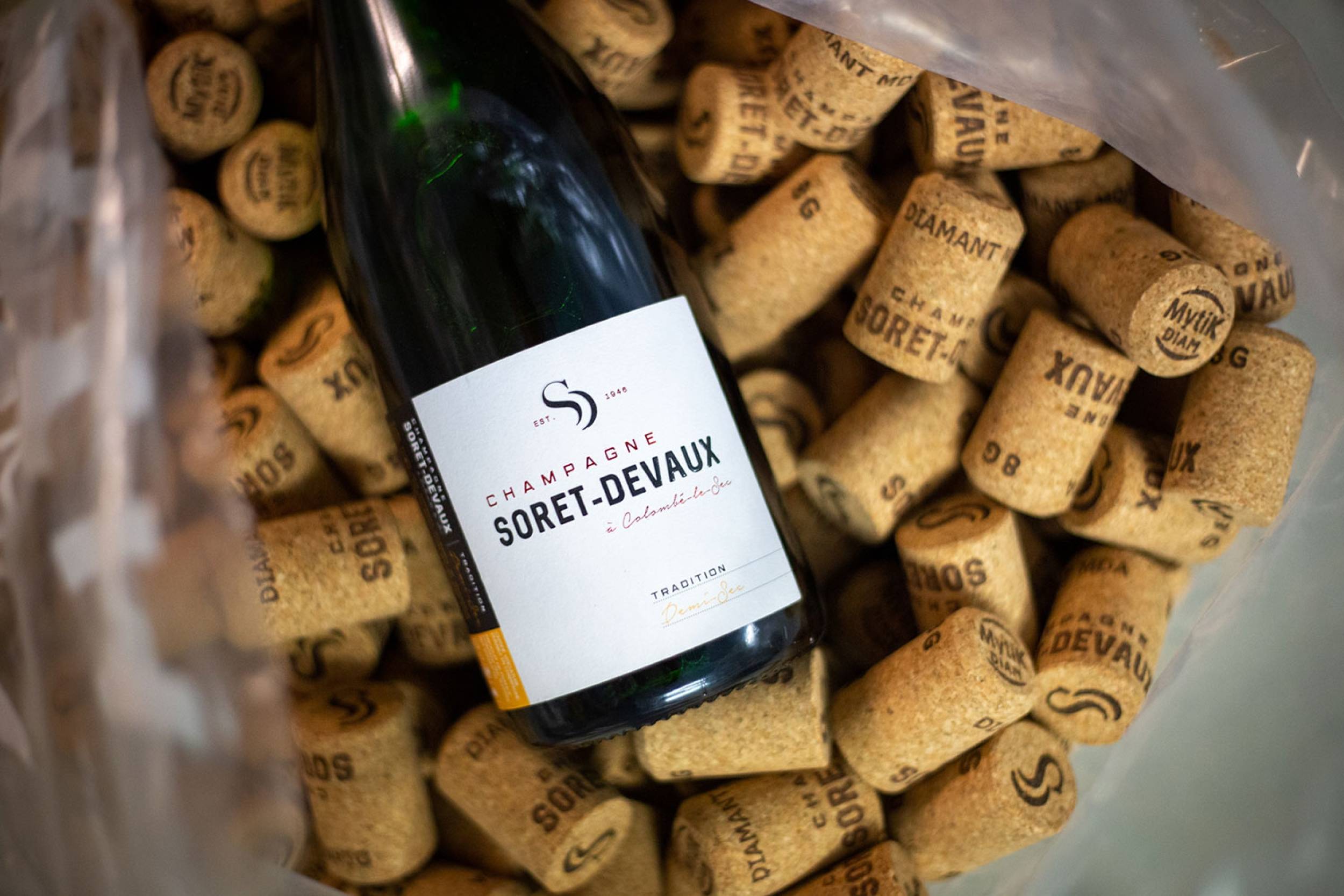 Vue rapprochée d'une bouteille de champagne Soret-Devaux posée sur des bouchons de champagne